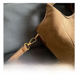 Close-up of golden metal hook and strap connection on brown suede handbag detail