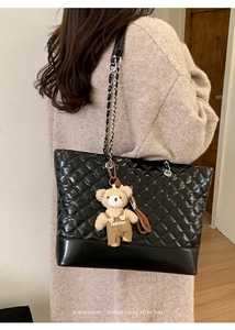 Detail of black quilted tote bag with chain strap and teddy bear fashion charm
