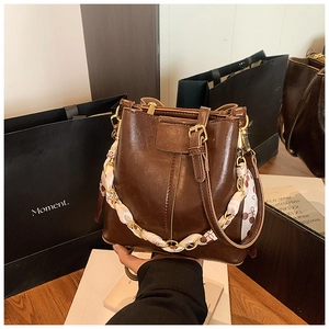 Detail of coffee brown bucket bag with silk scarf chain handle and shiny leather texture