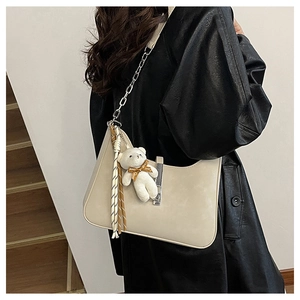 Detail of beige shoulder bag featuring silver buckle and cute white teddy bear charm