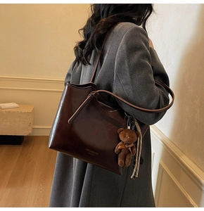 Close-up of a dark brown glossy tote bag with a cute plush bear charm on a grey winter coat