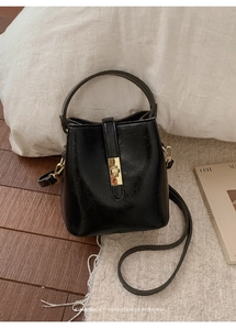 Retro black leather bucket bag with gold lock hardware on wood floor and white rug