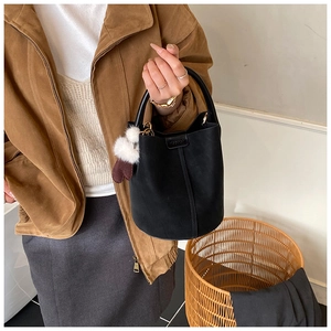Detail of black suede bucket bag featuring contrast stitching and a plush heart charm