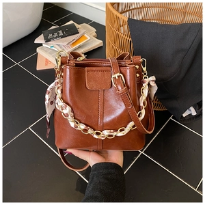Detail of vintage brown bucket bag with silk scarf wrapped chain handle and gold hardware