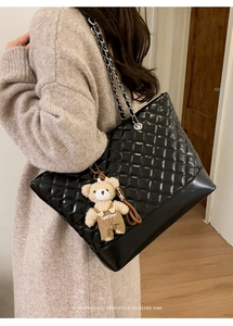 Detail of black quilted tote bag with silver chain strap and a cute bear charm