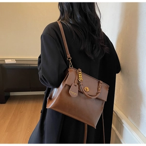 Detail of vintage brown leather handbag with gold twist lock and woven chain handle