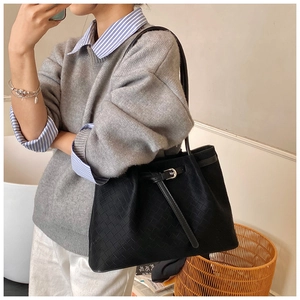 Detail of black woven tote bag with silver buckle worn by a model in casual setting
