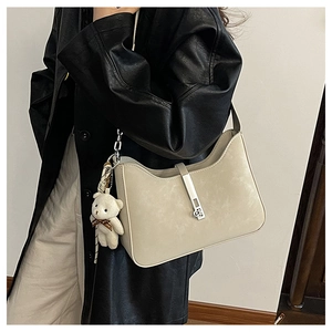 Detail of minimalist cream leather underarm bag with silver buckle and plush bear charm