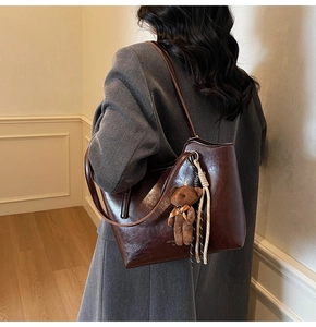 Brown leather tote bag featuring a plush bear pendant and dual-tone woven strap detail