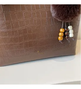 Detail of retro brown crocodile textured tote bag with brand logo and plush ball charm