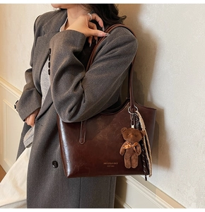 Detail of vintage dark brown leather tote bag featuring a teddy bear charm and striped scarf