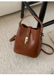 Detail of vintage brown oil wax leather bucket bag with gold twist lock on fuzzy rug