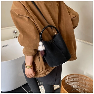 Detailed close-up of a black suede bucket bag featuring a white faux fur pompom charm