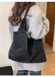 Detail of black suede tote bag with small zipper pouch shown from a side-back angle