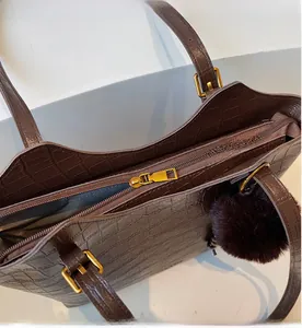 Detail of smooth metal zipper and crocodile embossed texture on brown tote bag