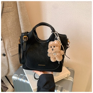 Detail of black suede shoulder bag with gold logo and plush bear charm on luggage