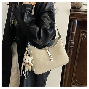Detail of cream shoulder bag with silver clasp and plush bear charm on black leather coat