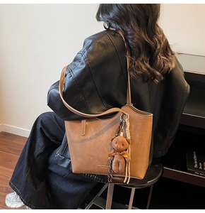 Brown tote bag detail with teddy bear charm shown on model in stylish street setting