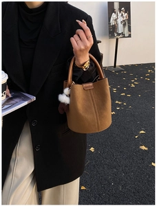 Close-up of brown suede bucket bag with dark handle and plush pompom charm detail