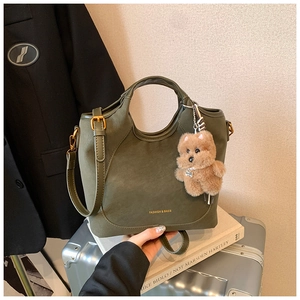 Detail of olive green suede bucket bag with round top handle and teddy bear charm