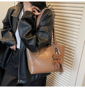Detail of vintage brown leather tote bag with logo and cute plush bear accessory
