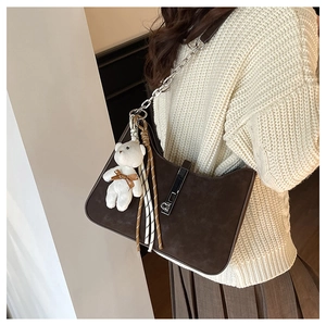 Detail of coffee brown suede crescent shoulder bag with bear charm and silver chain