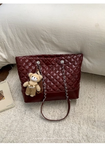 Macro shot of burgundy quilted patent leather tote bag with silver chain and teddy charm