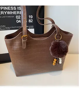 Macro detail of dark brown crocodile pattern tote bag with pompom charm and gold hardware