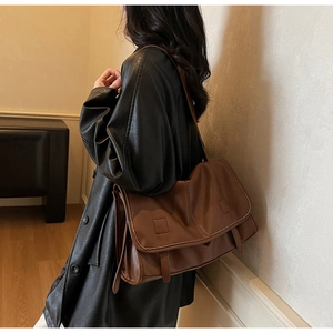 Detail view of a vintage dark brown leather messenger bag worn on a black leather jacket