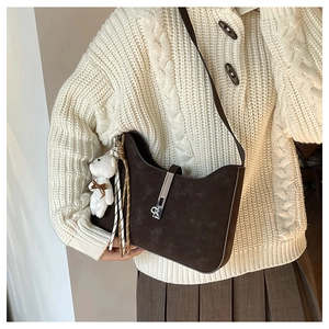 Detail of dark brown suede handbag with wave-shaped top, silver buckle, and bear charm