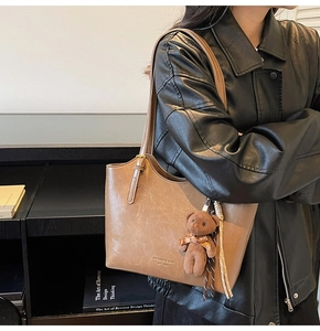 Close-up of brown leather tote bag featuring a cute teddy bear charm and logo detail