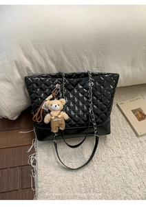 Close-up of black quilted tote bag with silver chain straps and a cute plush bear charm