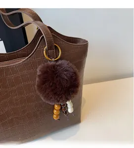 Detail of a plush brown bag charm with wooden beads on a faux crocodile leather bag