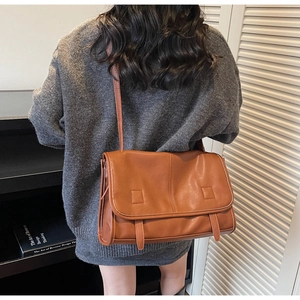 Detail view of caramel brown messenger bag with white piping and double strap accents