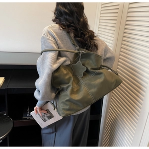 Deep green leather tote bag with contrast stitching and star charm shown on a model