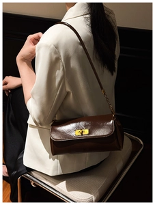 Detail of dark brown polished leather bag with golden metallic twist lock on white blazer