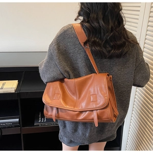 Detailed view of a vintage brown leather messenger bag with textured flap and square patches