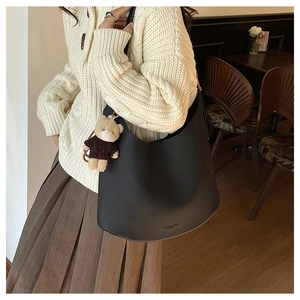 Gros plan d'un sac hobo noir avec pendentif ours sur un pull en maille douce