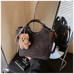 Close-up of brown suede bucket bag with gold lettering, leather handle and plush bear charm