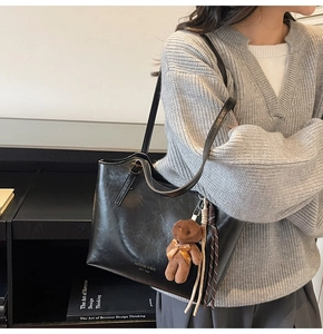 Detail of black leather tote bag with brown plush bear charm and woven tassel accent