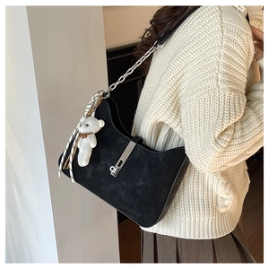 Black suede shoulder bag with chain strap and cute bear charm shown on a model