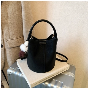 Detail of a black bucket bag with a plush charm on a cozy autumn coat background