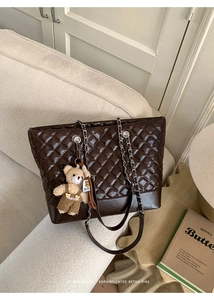 Close-up of dark brown quilted tote bag with silver chain strap and plush bear charm