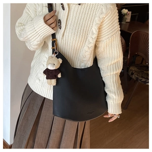 Détail du sac bandoulière demi-lune en cuir noir avec joli charme d'ours en peluche