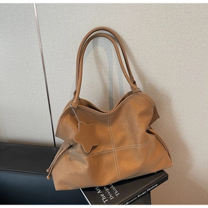 Detail of caramel leather tote bag with white contrast stitching and star charm accessory