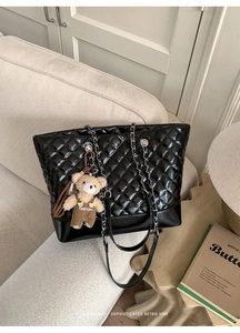 Detail of black quilted tote bag featuring silver chain strap and a cute bear charm