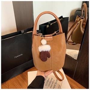 Brown faux suede bucket bag with a cute plush glove charm on a wooden table detail
