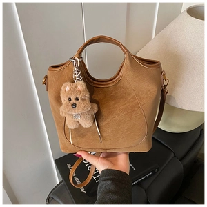 Detail of a dark brown suede bucket bag featuring a plush puppy charm and golden hardware