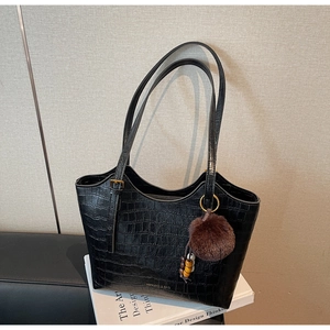 Detail of black crocodile embossed tote bag with faux fur pompom and gold buckles