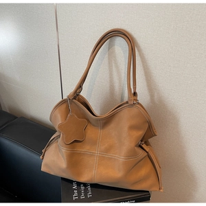 Close-up of brown leather tote bag with white contrast stitching and star charm detail